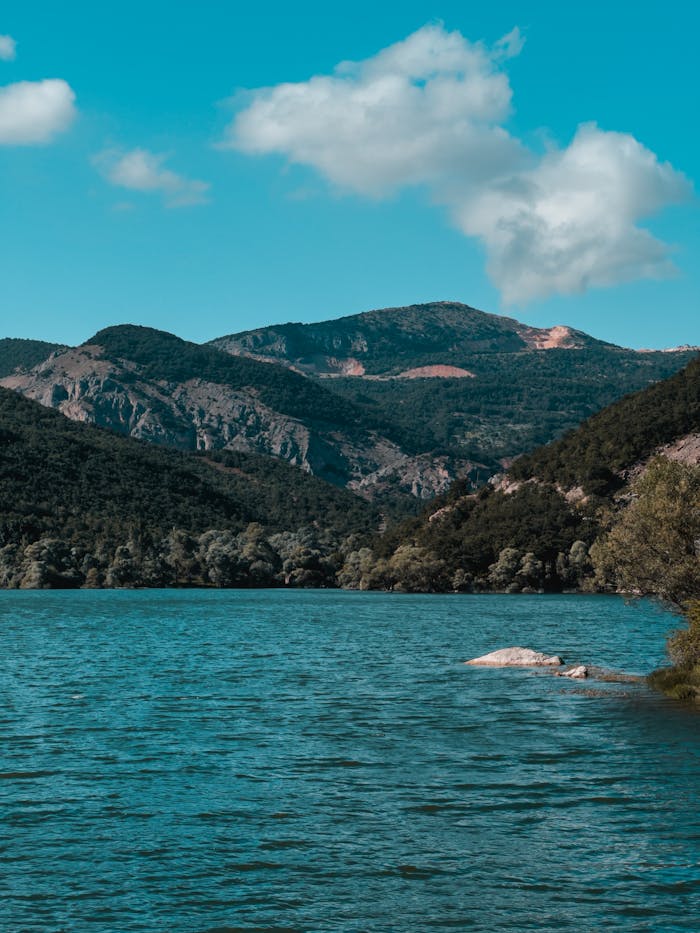 Beautiful mountain landscape with turquoise lake and lush greenery under a bright sky.